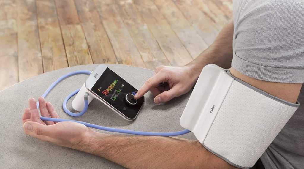 A person using a digital blood pressure monitor with a white cuff on their arm, adjusting the device's screen.