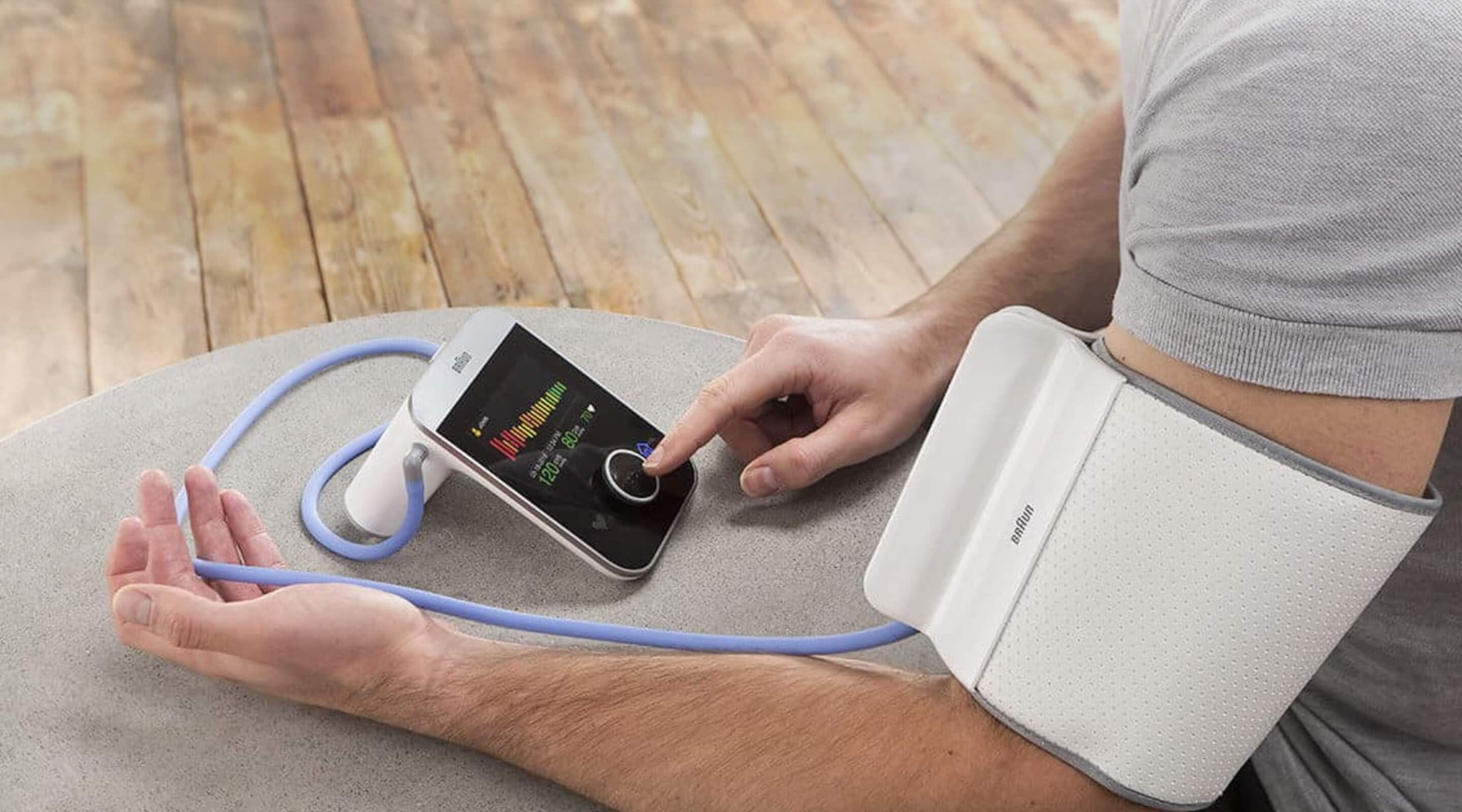 A person using a digital blood pressure monitor with a white cuff on their arm, adjusting the device's screen.
